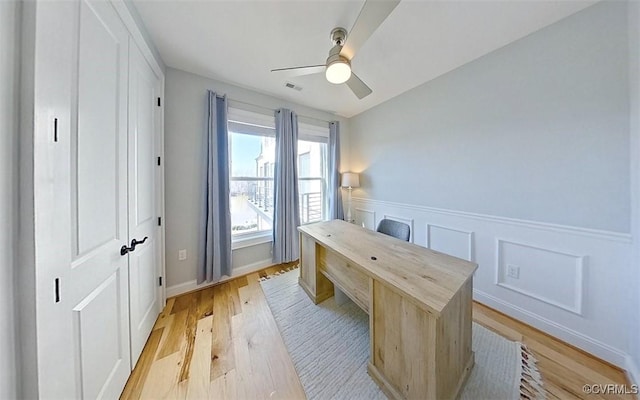 office featuring a wainscoted wall, light wood-type flooring, visible vents, and a ceiling fan