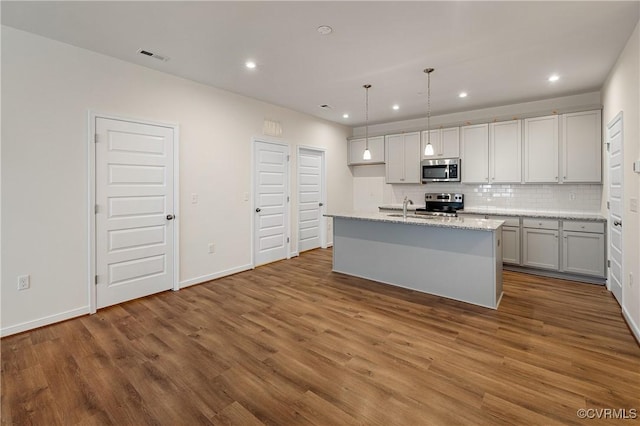 kitchen with a center island with sink, wood-type flooring, stainless steel appliances, decorative light fixtures, and sink