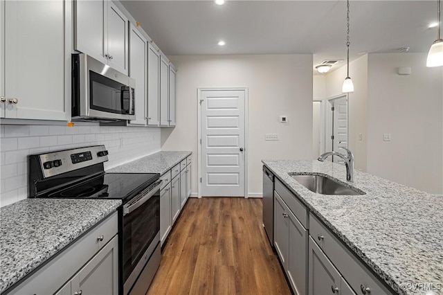 kitchen with appliances with stainless steel finishes, sink, decorative light fixtures, light stone countertops, and tasteful backsplash