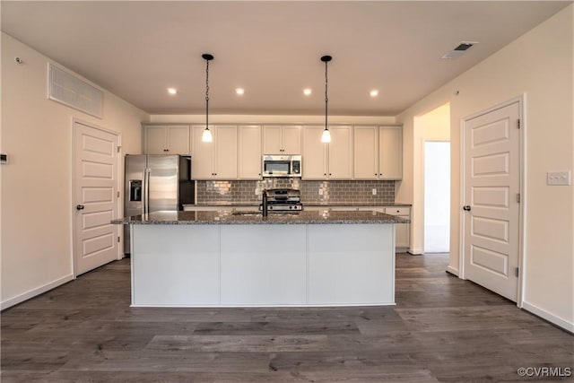 kitchen with dark stone countertops, white cabinetry, stainless steel appliances, hanging light fixtures, and a kitchen island with sink