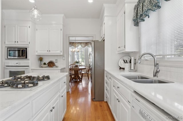 kitchen with stainless steel appliances, light countertops, hanging light fixtures, white cabinetry, and a sink