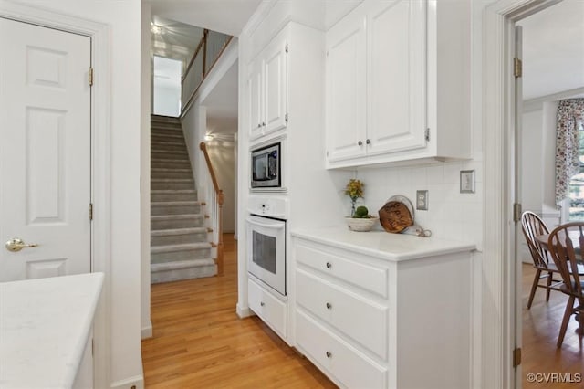 kitchen with white oven, white cabinets, light countertops, and stainless steel microwave