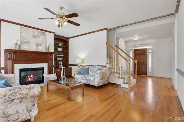 living area with crown molding, stairway, a premium fireplace, light wood-type flooring, and baseboards