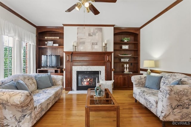 living area featuring light wood-type flooring, built in features, a high end fireplace, and crown molding