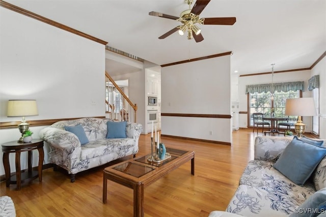 living area featuring baseboards, a ceiling fan, stairway, crown molding, and light wood-style floors