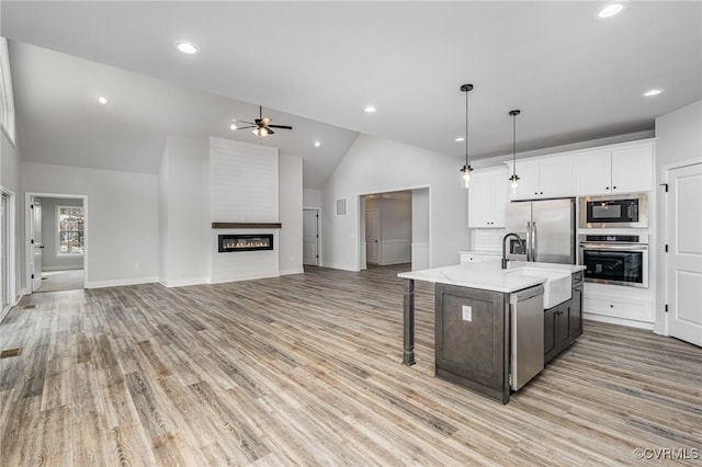 kitchen featuring a center island with sink, sink, stainless steel appliances, white cabinets, and hanging light fixtures