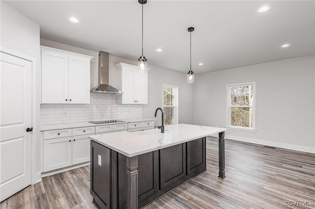 kitchen featuring wall chimney exhaust hood, white cabinetry, a kitchen island with sink, and hanging light fixtures