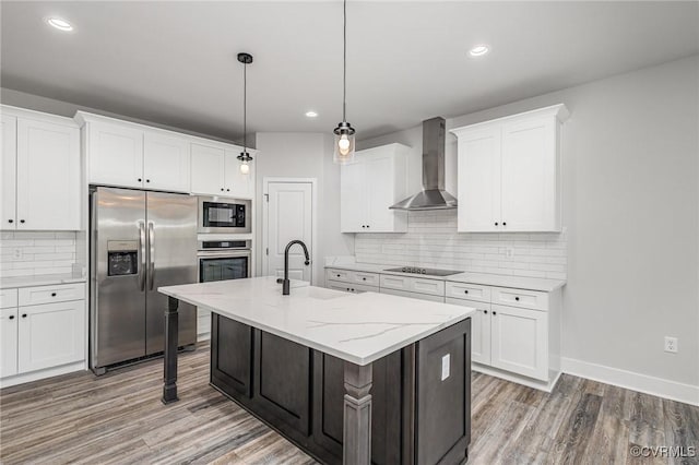 kitchen with an island with sink, white cabinets, black appliances, wall chimney range hood, and sink