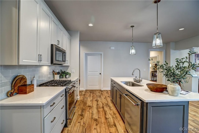 kitchen with a center island with sink, stainless steel appliances, decorative light fixtures, sink, and backsplash