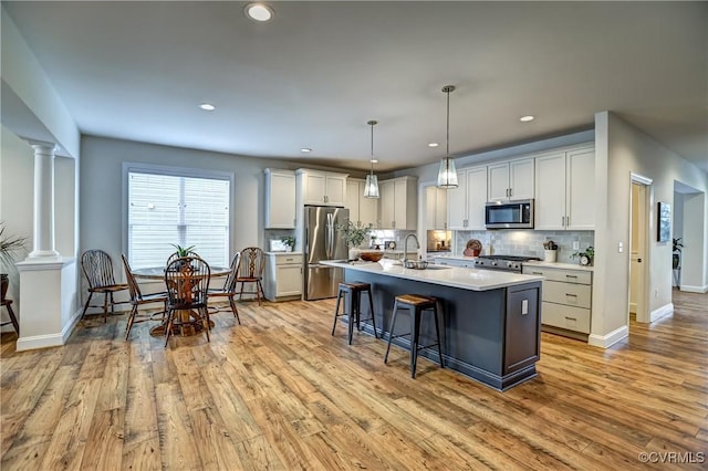 kitchen featuring appliances with stainless steel finishes, an island with sink, decorative light fixtures, sink, and decorative columns