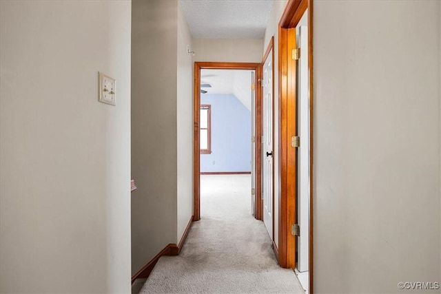 hall featuring a textured ceiling, light colored carpet, and lofted ceiling