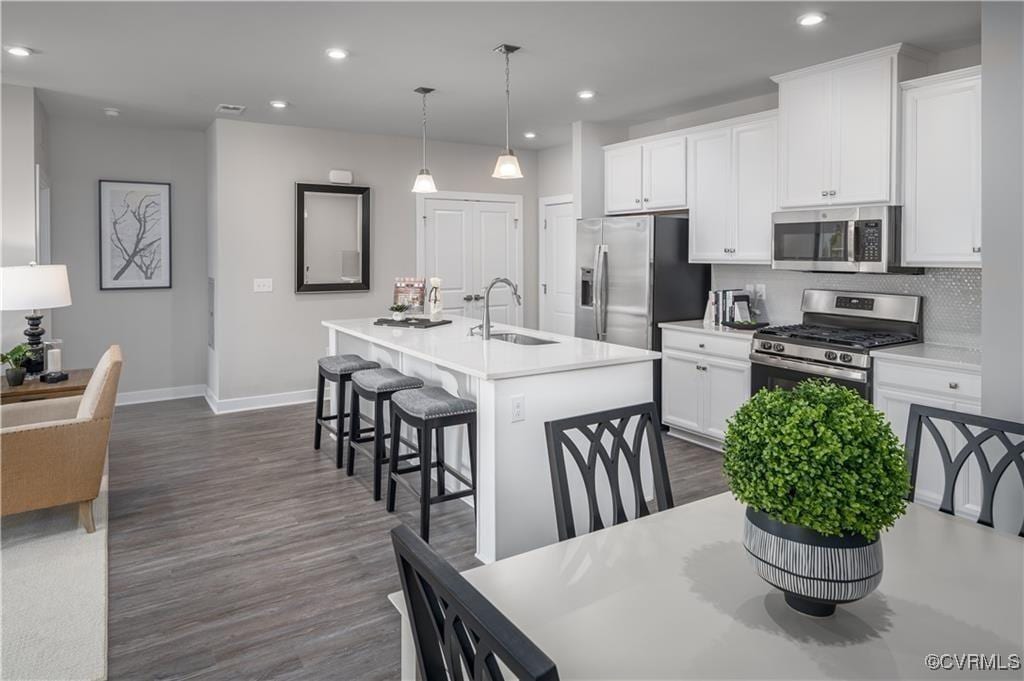 kitchen featuring appliances with stainless steel finishes, a center island with sink, white cabinets, decorative light fixtures, and sink