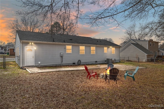 back of house at dusk with an outdoor fire pit, crawl space, central AC unit, and fence