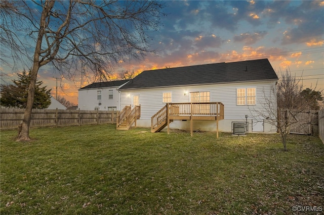 back house at dusk featuring a deck and a lawn