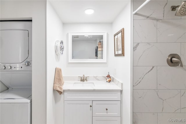 bathroom featuring toilet, tiled shower, vanity, and stacked washer and clothes dryer