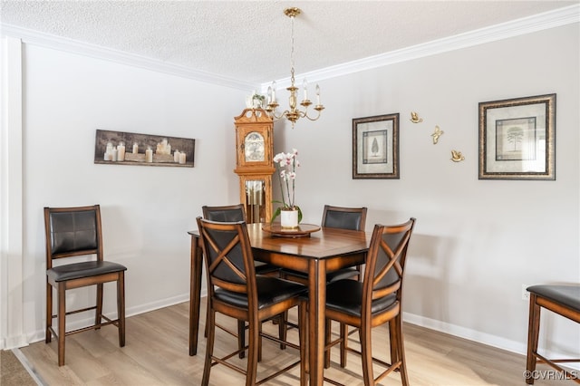 dining room with ornamental molding, light wood-style floors, a textured ceiling, and an inviting chandelier