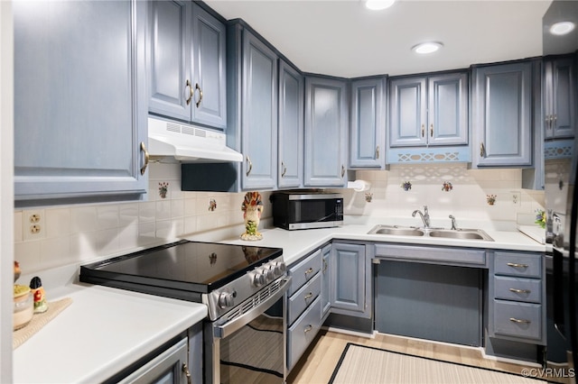 kitchen with light countertops, backsplash, appliances with stainless steel finishes, a sink, and under cabinet range hood