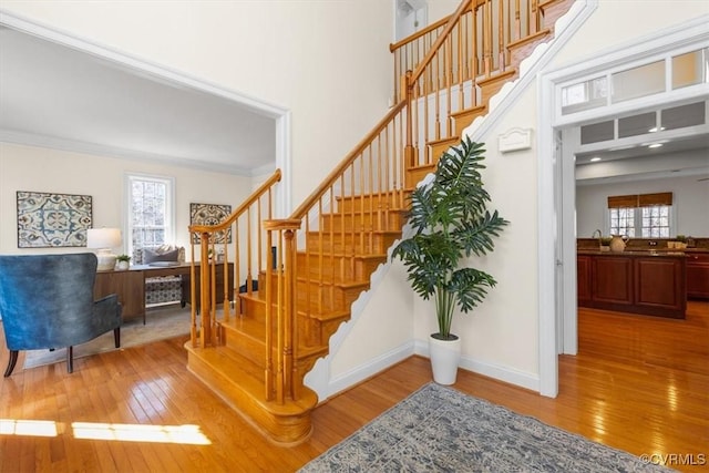 stairs featuring a wealth of natural light, wood-type flooring, crown molding, and baseboards