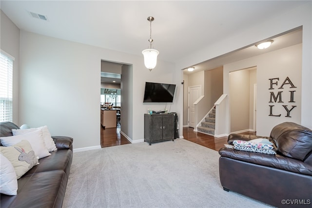 living area featuring dark colored carpet, stairway, baseboards, and visible vents