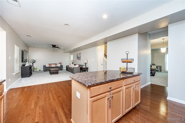 kitchen featuring visible vents, light brown cabinets, dark stone counters, wood finished floors, and a ceiling fan