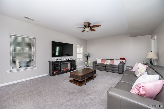 carpeted living area featuring visible vents, baseboards, a warm lit fireplace, and ceiling fan