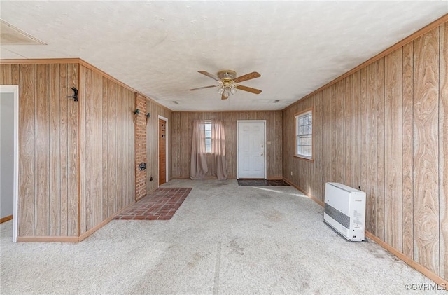 carpeted empty room with heating unit, ceiling fan, and wood walls