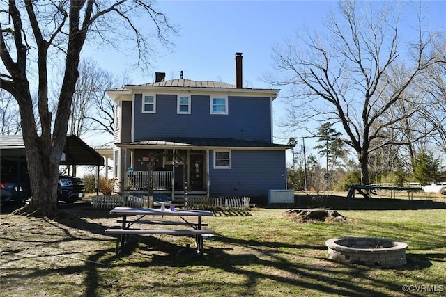 back of property with a yard, a chimney, a porch, metal roof, and a fire pit