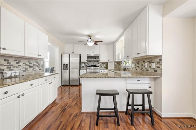 kitchen featuring a peninsula, dark wood-style flooring, a sink, stainless steel appliances, and white cabinets