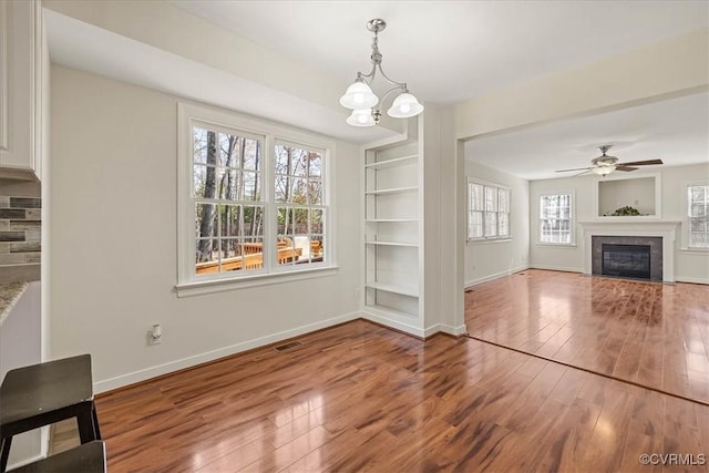 unfurnished living room with visible vents, ceiling fan with notable chandelier, hardwood / wood-style floors, a fireplace, and baseboards