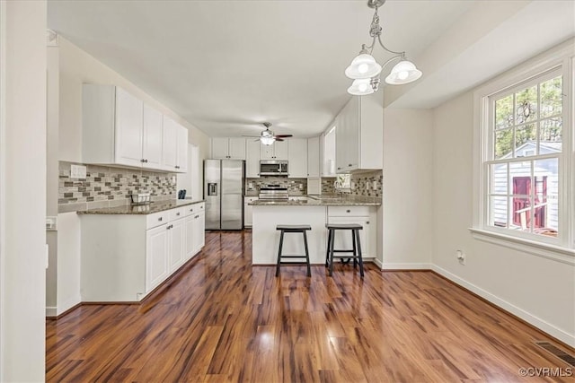 kitchen with stainless steel appliances, a peninsula, dark wood-style floors, and white cabinets