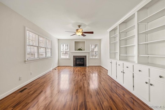 unfurnished living room with a ceiling fan, visible vents, wood finished floors, baseboards, and a fireplace with flush hearth