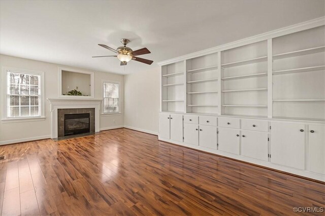 unfurnished living room with a ceiling fan, wood finished floors, baseboards, and a tile fireplace