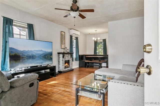 living room featuring a wealth of natural light, wood finished floors, a stone fireplace, and a wall mounted AC