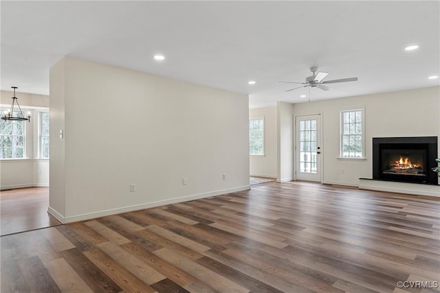 unfurnished living room featuring ceiling fan with notable chandelier and dark wood-type flooring