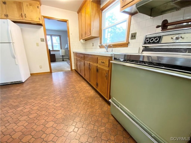 kitchen featuring range, white refrigerator, range hood, sink, and backsplash