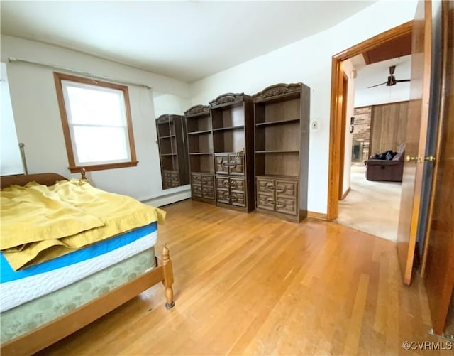 bedroom with a stone fireplace, a baseboard radiator, and hardwood / wood-style floors