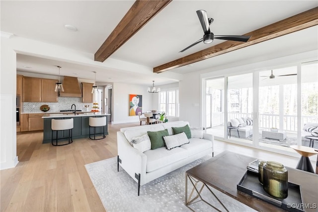 living room with sink, ceiling fan with notable chandelier, light hardwood / wood-style floors, and beam ceiling