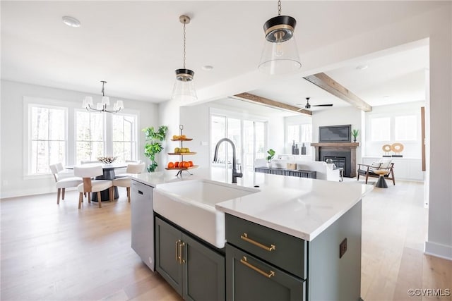 kitchen with a kitchen island with sink, beam ceiling, sink, stainless steel dishwasher, and pendant lighting