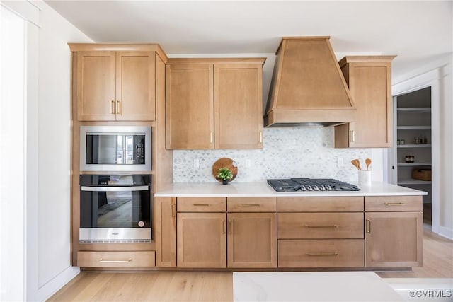 kitchen with appliances with stainless steel finishes, decorative backsplash, light hardwood / wood-style floors, and premium range hood