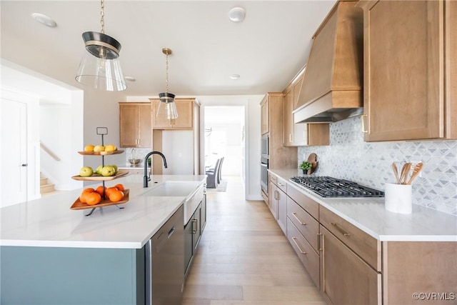 kitchen with a center island with sink, sink, premium range hood, decorative light fixtures, and stainless steel appliances