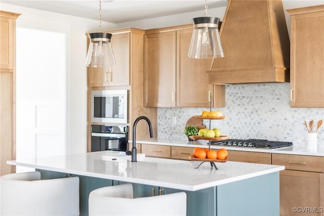 kitchen featuring appliances with stainless steel finishes, a center island with sink, wall chimney exhaust hood, decorative light fixtures, and backsplash