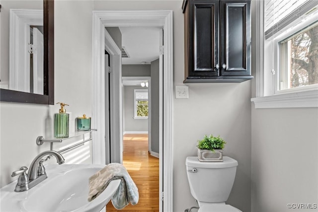 half bath featuring toilet, a sink, visible vents, wood finished floors, and baseboards