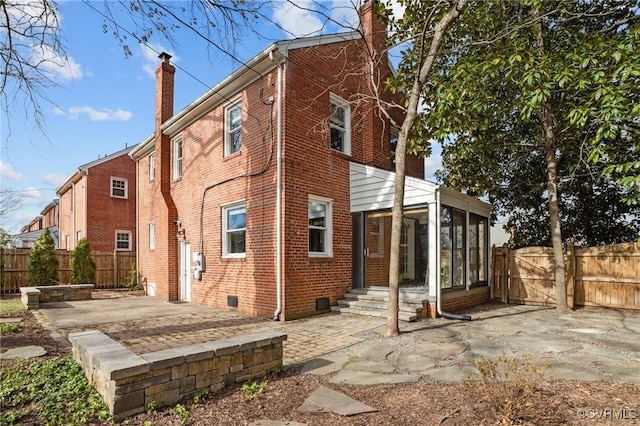 back of property featuring a sunroom, brick siding, a patio, and a chimney