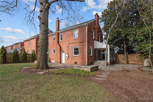 rear view of property with a fenced backyard, a chimney, a yard, a patio area, and brick siding