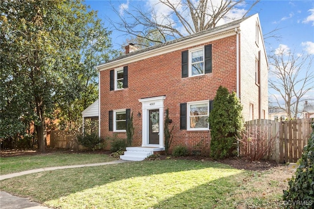 colonial inspired home featuring brick siding, a front lawn, a chimney, and fence