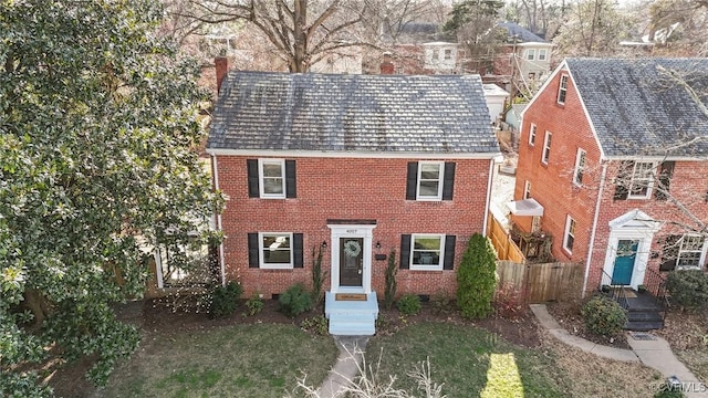 colonial-style house featuring brick siding, a front lawn, a chimney, and fence