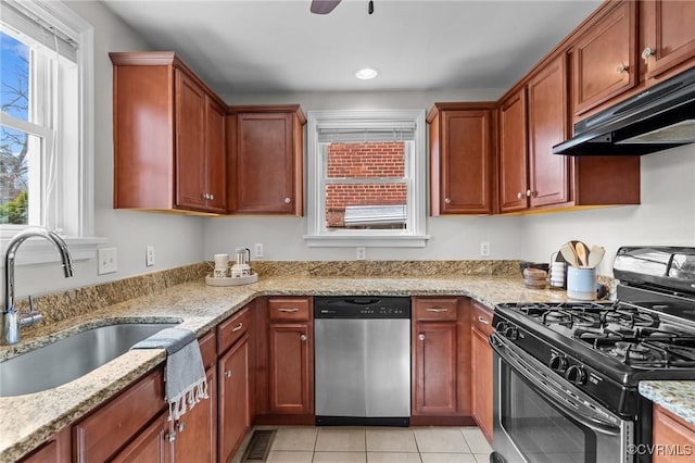 kitchen featuring light tile patterned floors, appliances with stainless steel finishes, light stone countertops, under cabinet range hood, and a sink