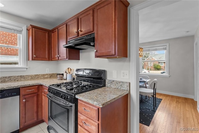 kitchen with under cabinet range hood, stainless steel appliances, baseboards, light stone countertops, and light wood finished floors