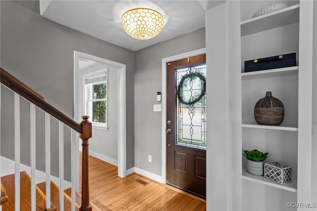 foyer entrance with baseboards, visible vents, stairway, and wood finished floors