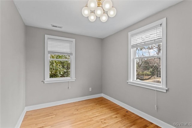 spare room featuring an inviting chandelier, baseboards, visible vents, and wood finished floors